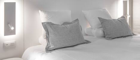 A modern bedroom with a large bed, two bedside tables, and a wall-mounted light fixture.
