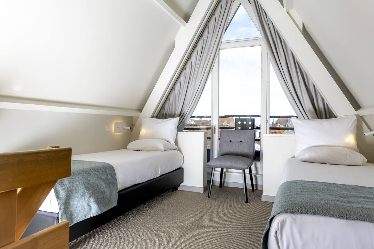 Une chambre à coucher moderne, de forme triangulaire, comprenant deux lits, un bureau et une chaise.