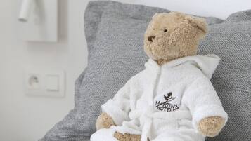 A teddy bear in a white robe sitting on a bed with gray pillows.