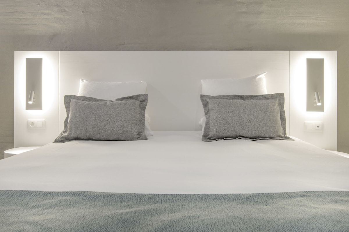 Une chambre d’hôtel moderne avec un grand lit, deux tables de chevet et des lampes fixées au mur.