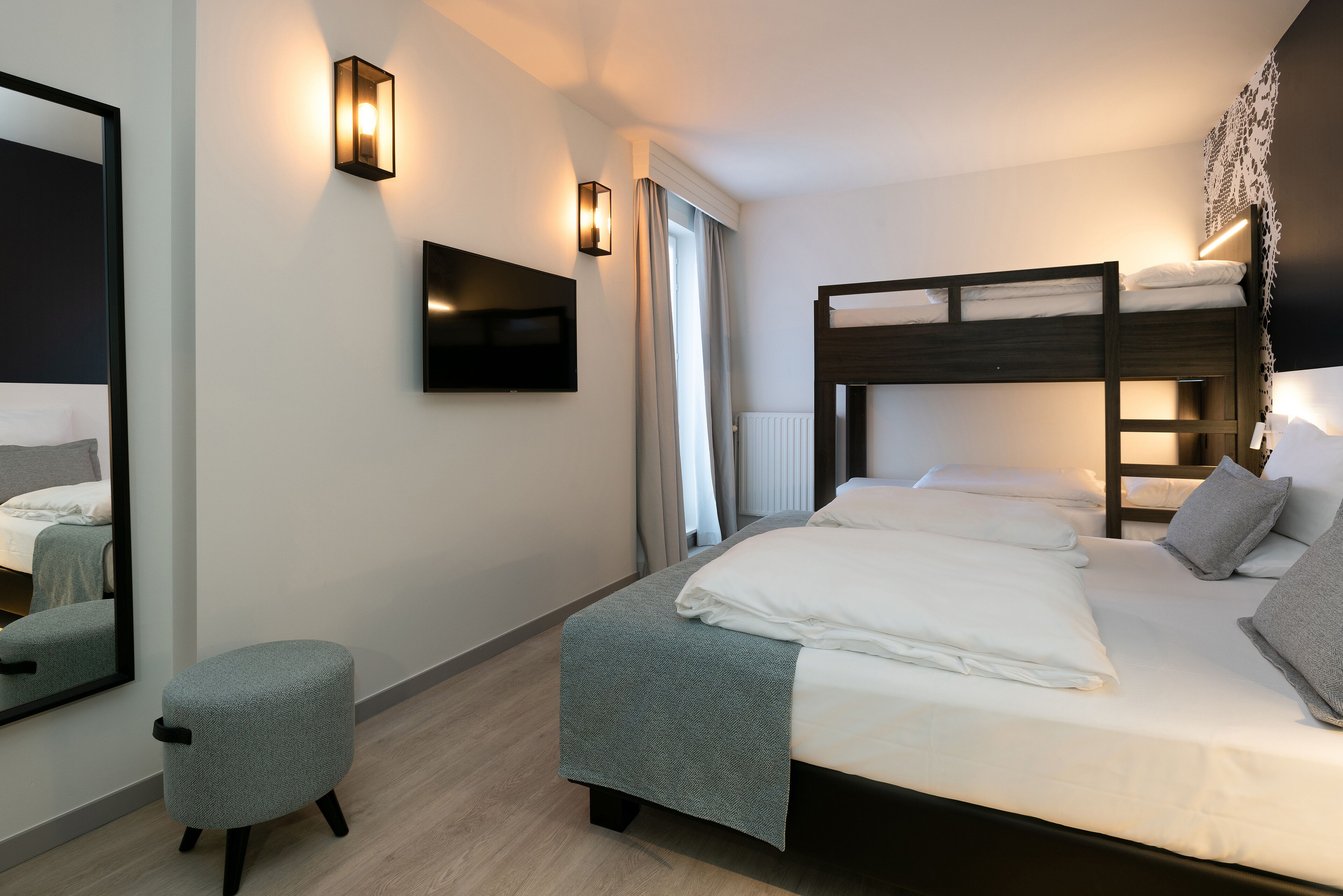A modern hotel room with a large bed, a small seating area, and a TV mounted on the wall.