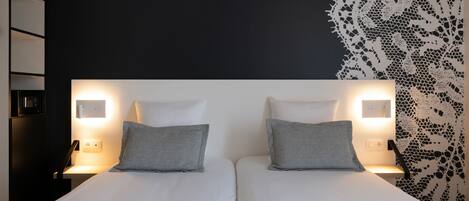 Un lit double avec deux oreillers, des tables de chevet avec des lampes, un mur à motifs noir et blanc et une tête de lit sombre.