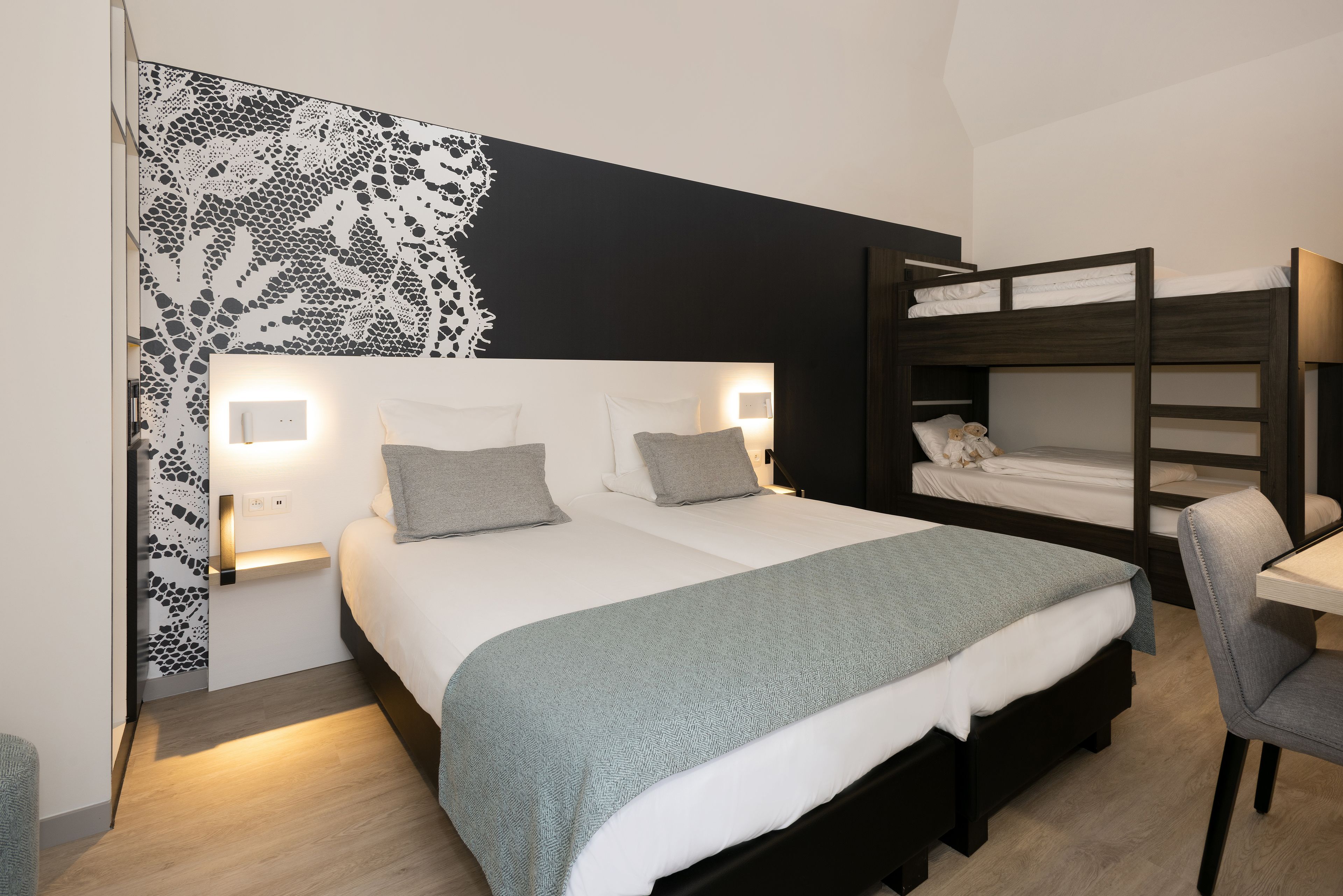 Un dormitorio con una cama litera, una mesita de noche y una lámpara fijada a la pared.