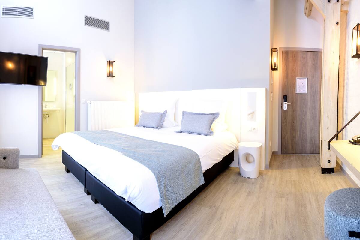 Une chambre d’hôtel moderne avec un grand lit, des tables de chevet, un petit tabouret, un bureau et une chaise.
