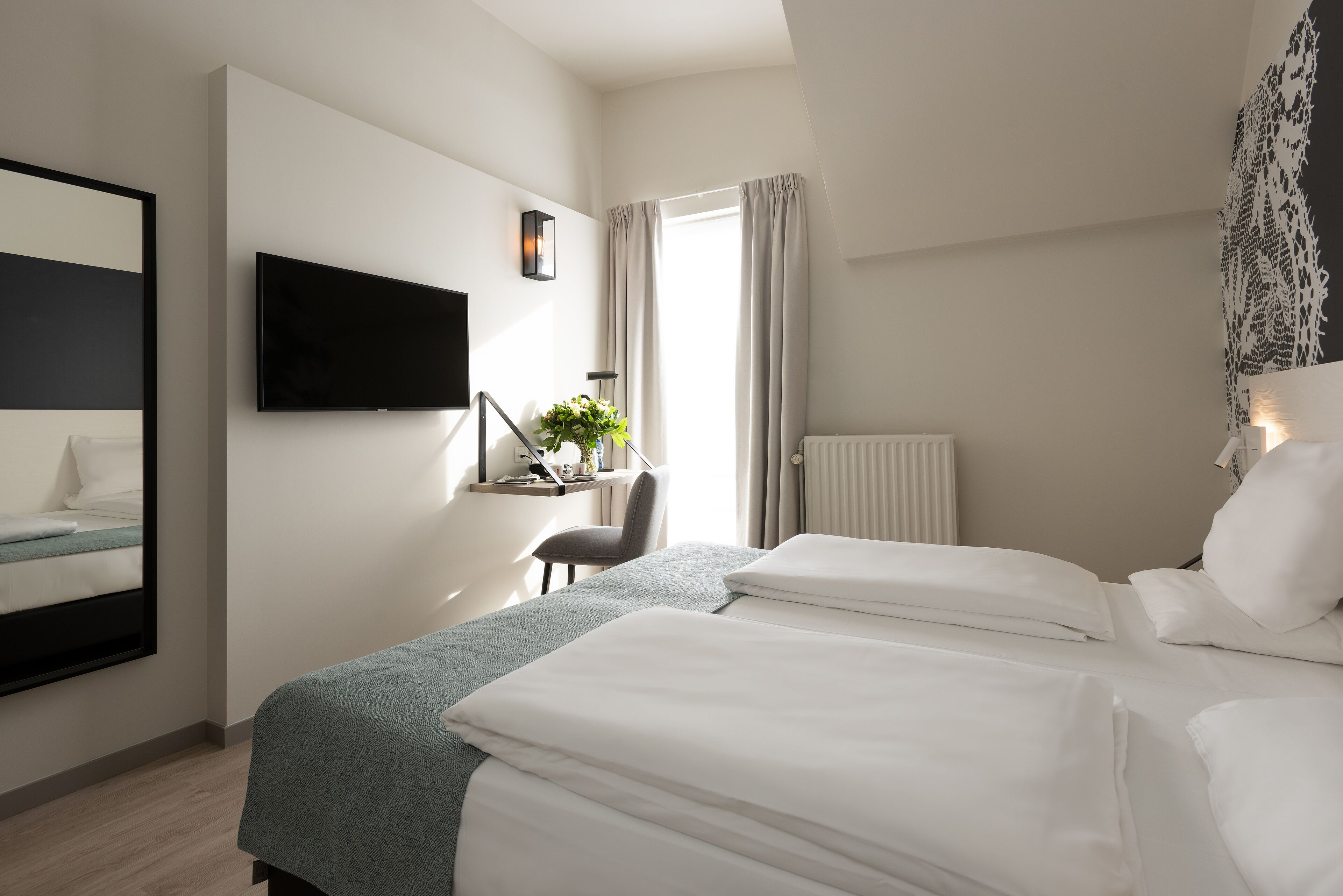 A hotel room with two beds, a desk, a chair, a TV, and a window with curtains.