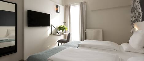 A hotel room with two beds, a desk, a chair, a TV, and a window with curtains.