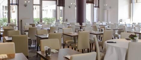 A spacious dining area with multiple tables and chairs, large windows, and a modern interior design.