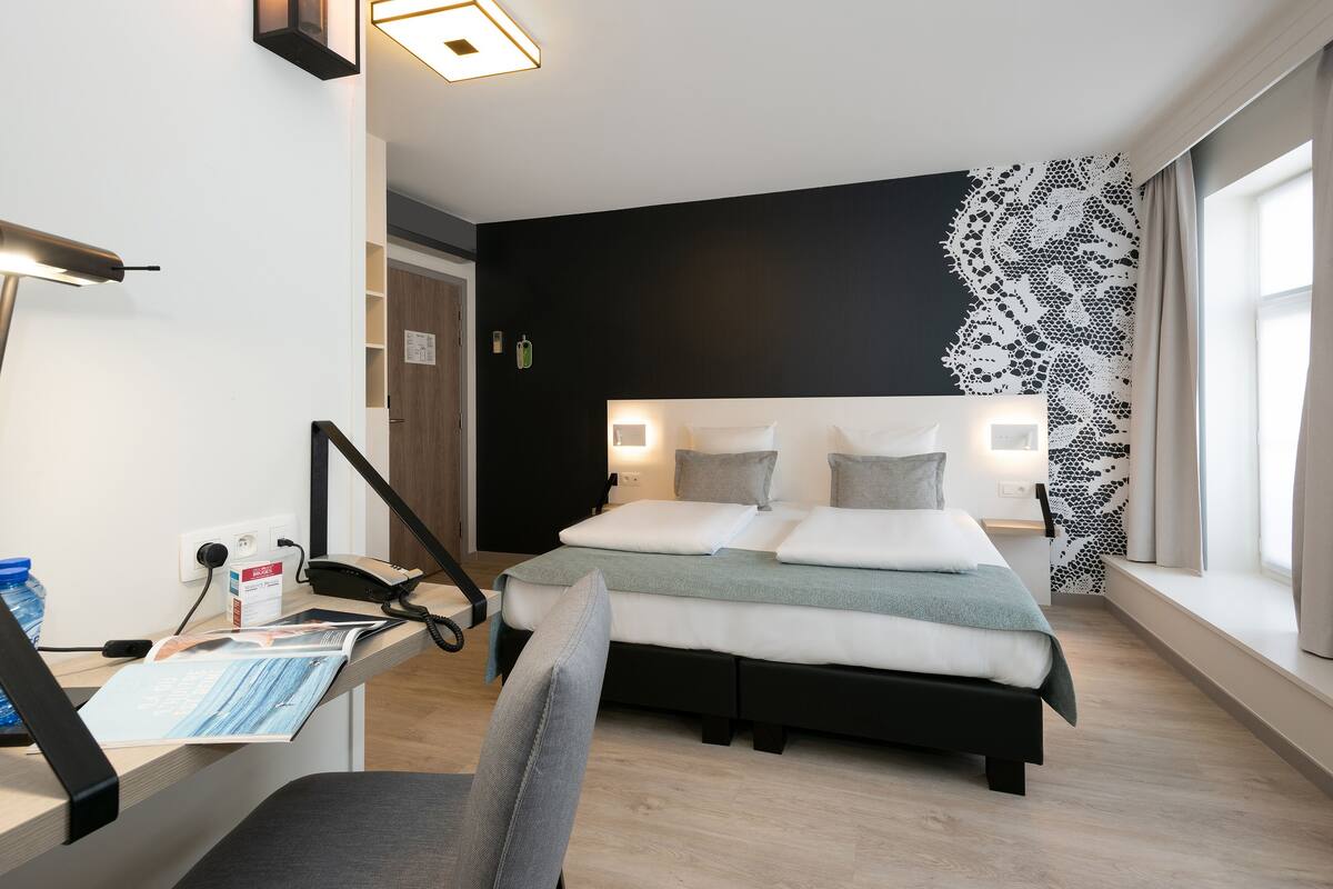 Une chambre d’hôtel moderne avec un grand lit, un bureau équipé d’un ordinateur et une fenêtre donnant sur un beau paysage.