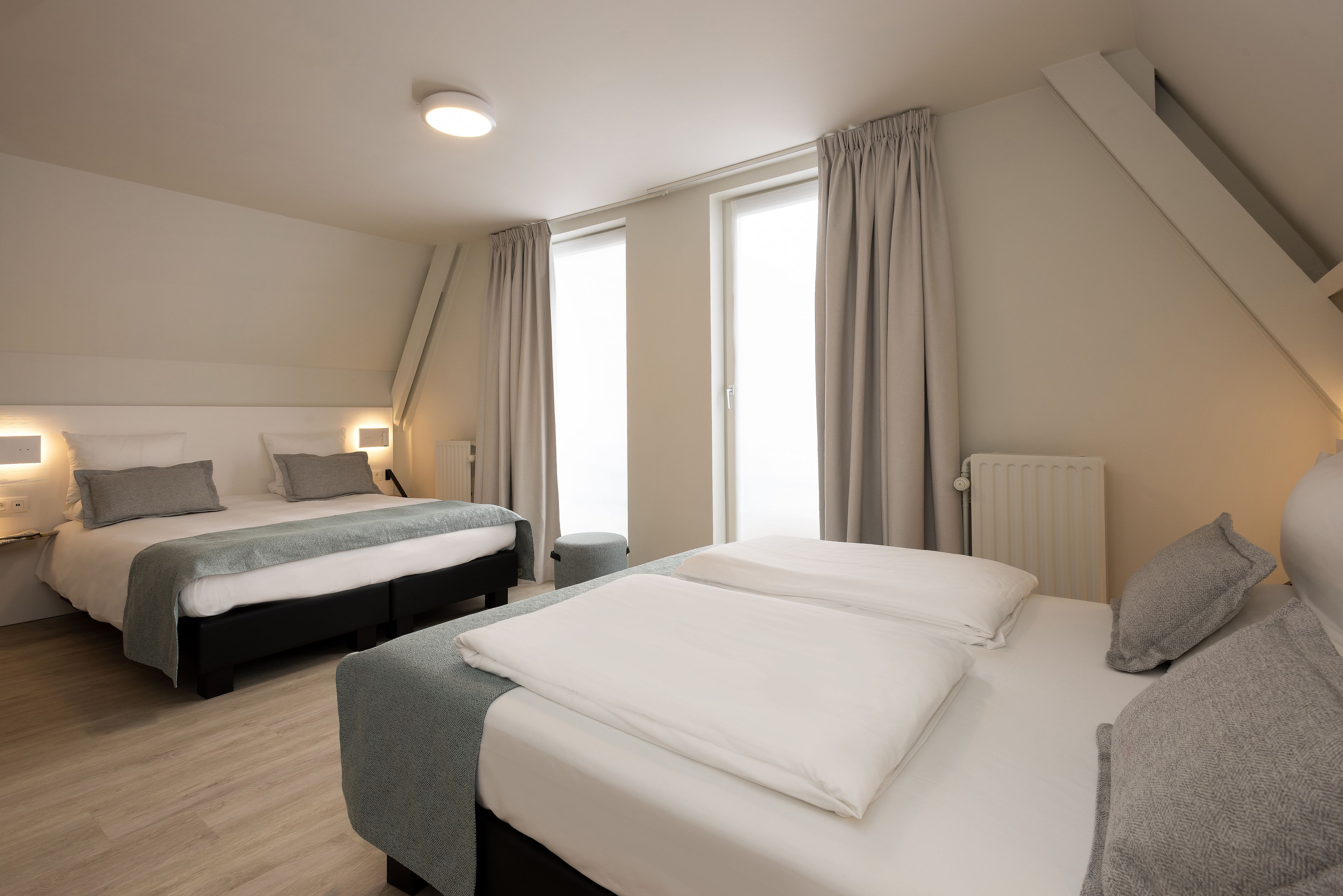 Ett modernt hotellrum med två sängar, en liten sittgrupp och ett stort fönster med gardiner.