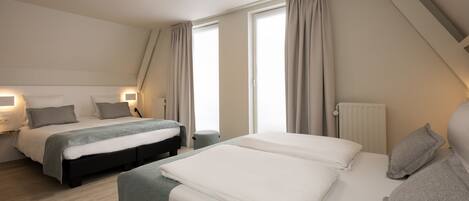 A modern hotel room with two beds, a small seating area, and a large window with curtains.