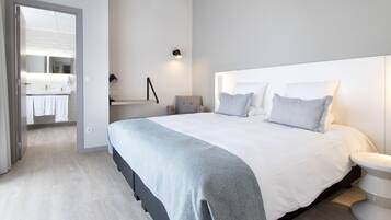 A modern bedroom with a large bed, bedside tables, a nightstand, and a bathroom visible through an open door.