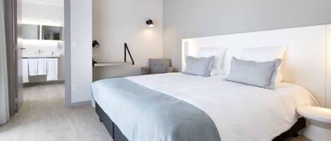 A modern bedroom with a large bed, bedside tables, a nightstand, and a bathroom visible through an open door.