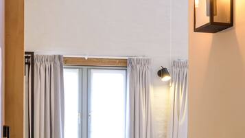 A bedroom with a sloped ceiling, a small skylight, a bed, a bench, a desk, and a wall-mounted light fixture.
