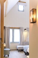 A bedroom with a sloped ceiling, a small skylight, a bed, a bench, a desk, and a wall-mounted light fixture.