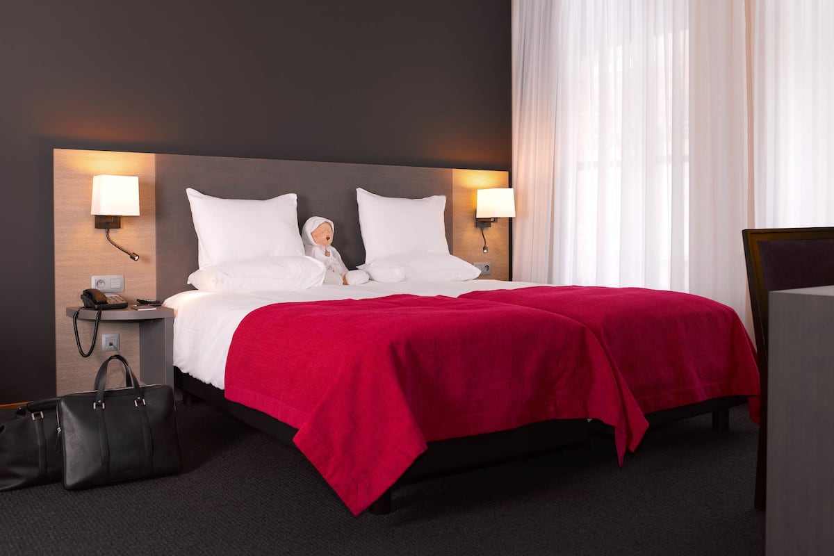 Une chambre d’hôtel avec un lit, deux lampes de chevet, une table de chevet avec un téléphone et une couverture rouge.