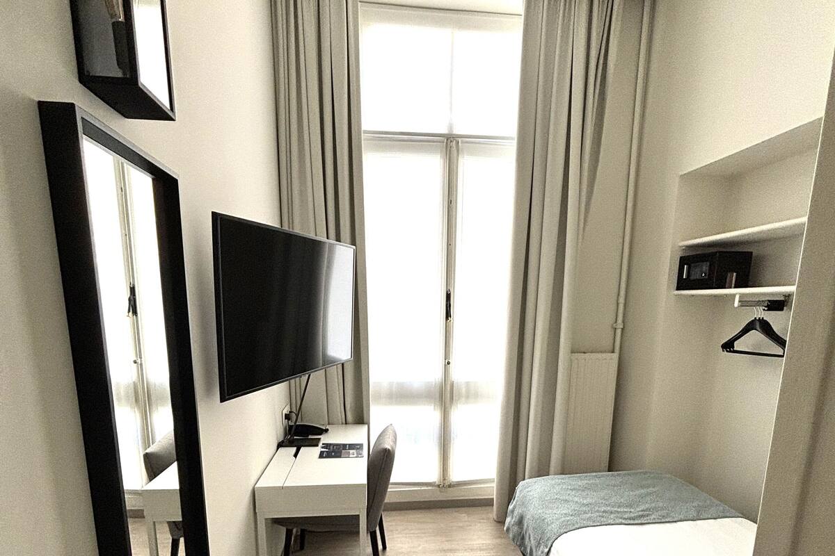Une chambre d’hôtel comprenant un lit, un bureau avec une chaise, une télévision et une fenêtre avec des rideaux.