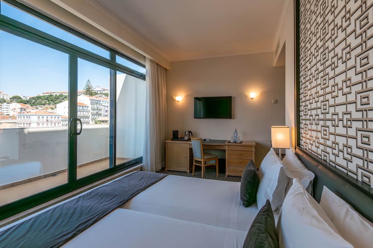 A hotel room with a bed, desk, chair, and a TV on the wall.