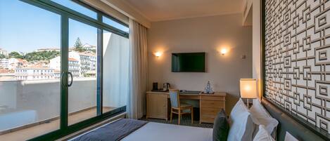 A hotel room with a bed, desk, chair, and a TV on the wall.