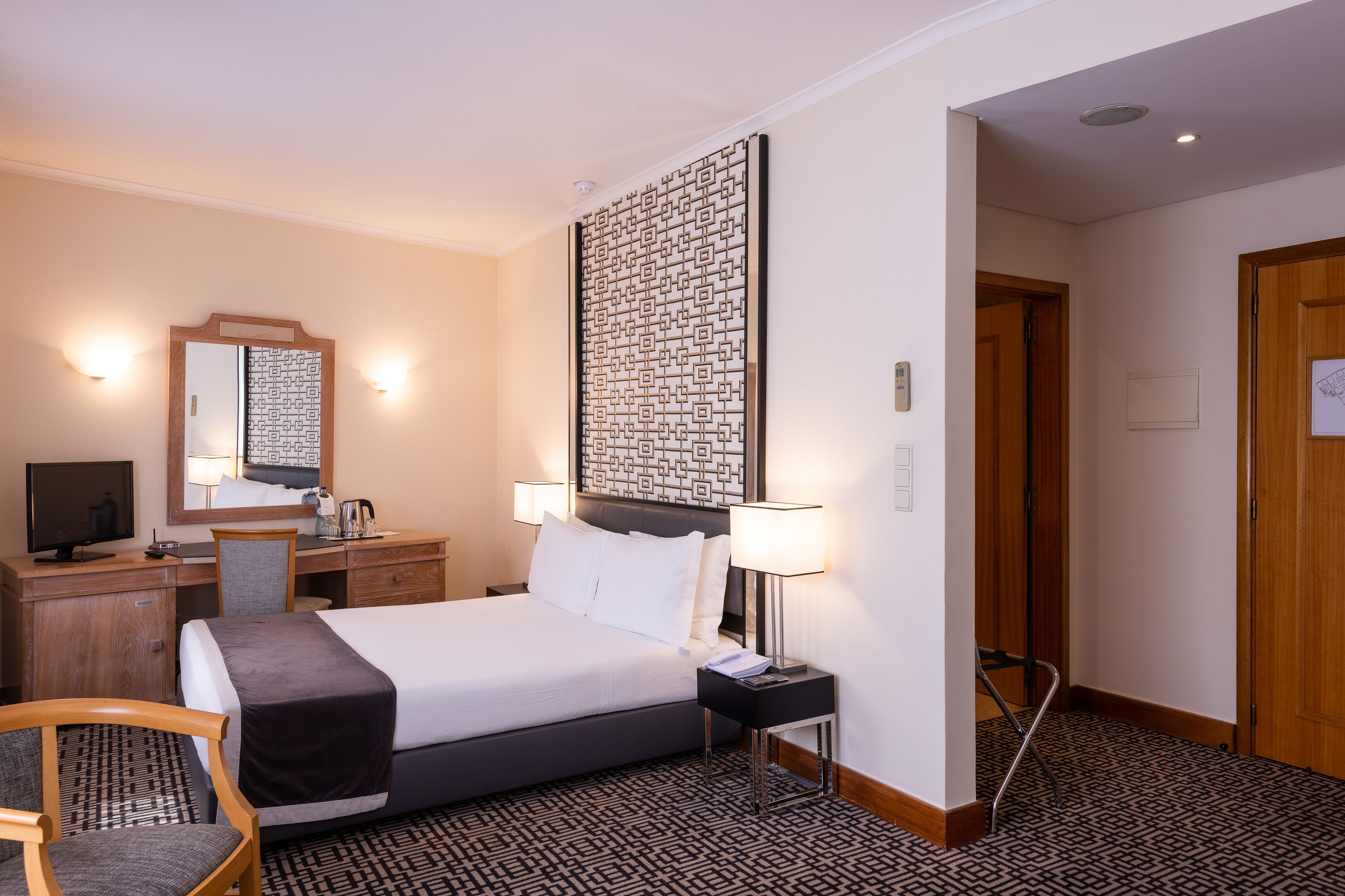Habitación de hotel con cama, escritorio, silla y un gran elemento decorativo en la pared.