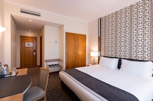 A hotel room with a bed, a desk with a chair, a lamp, and a patterned wall.