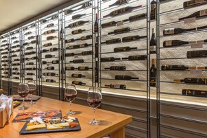 Una cantina vinicola con numerose bottiglie sugli scaffali e un tavolo con bicchieri da vino e taglieri di formaggio.