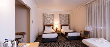A hotel room with two beds, a desk with a water bottle and glasses, and a chair.