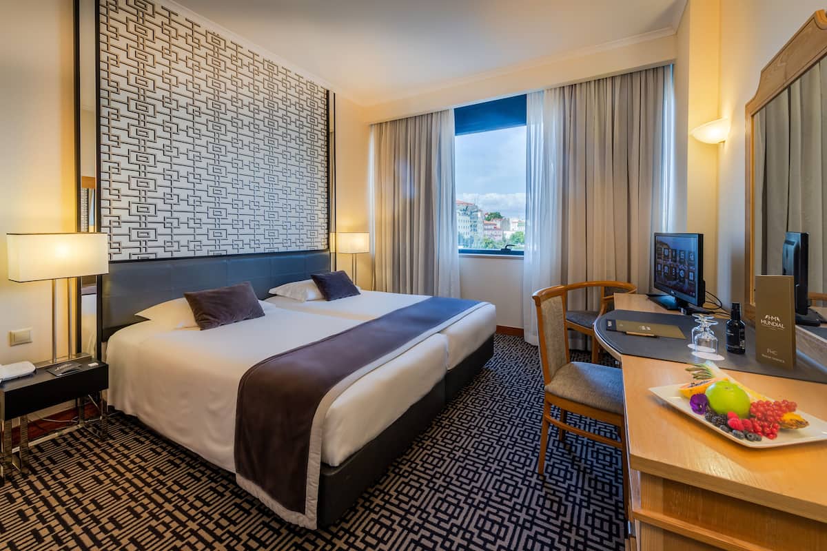 A hotel room with a large bed, a desk with a computer, a chair, and a fruit platter on the desk.