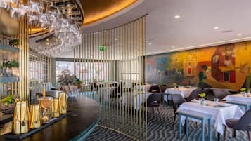 A restaurant with a modern interior, featuring a bar area with a unique glassware display, tables set for dining, and a colorful mural on the wall.