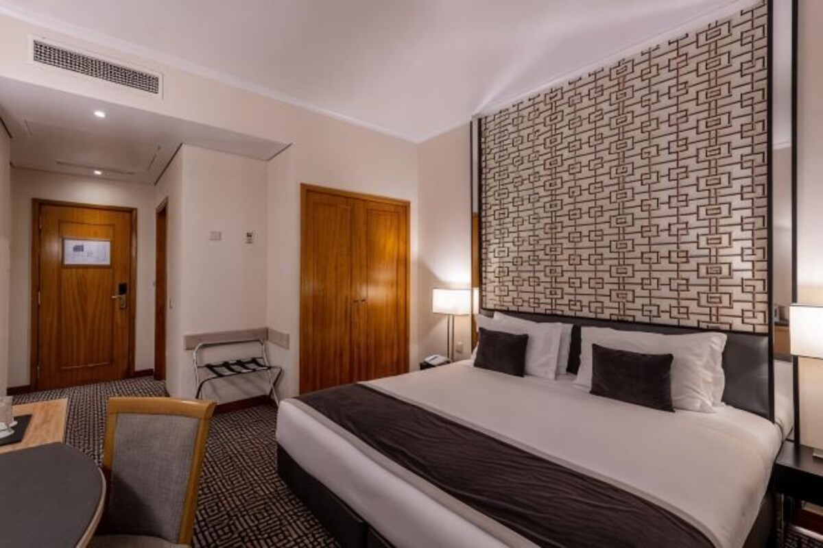 Habitación de hotel con una cama grande, un escritorio, una silla, un televisor instalado en la pared y un papel tapiz estampado.