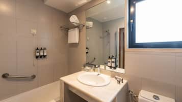 Une salle de bain moderne avec une baignoire, un lavabo et des toilettes. On y trouve un porte-serviettes avec une serviette, une barre d’appui et un miroir au-dessus du lavabo.