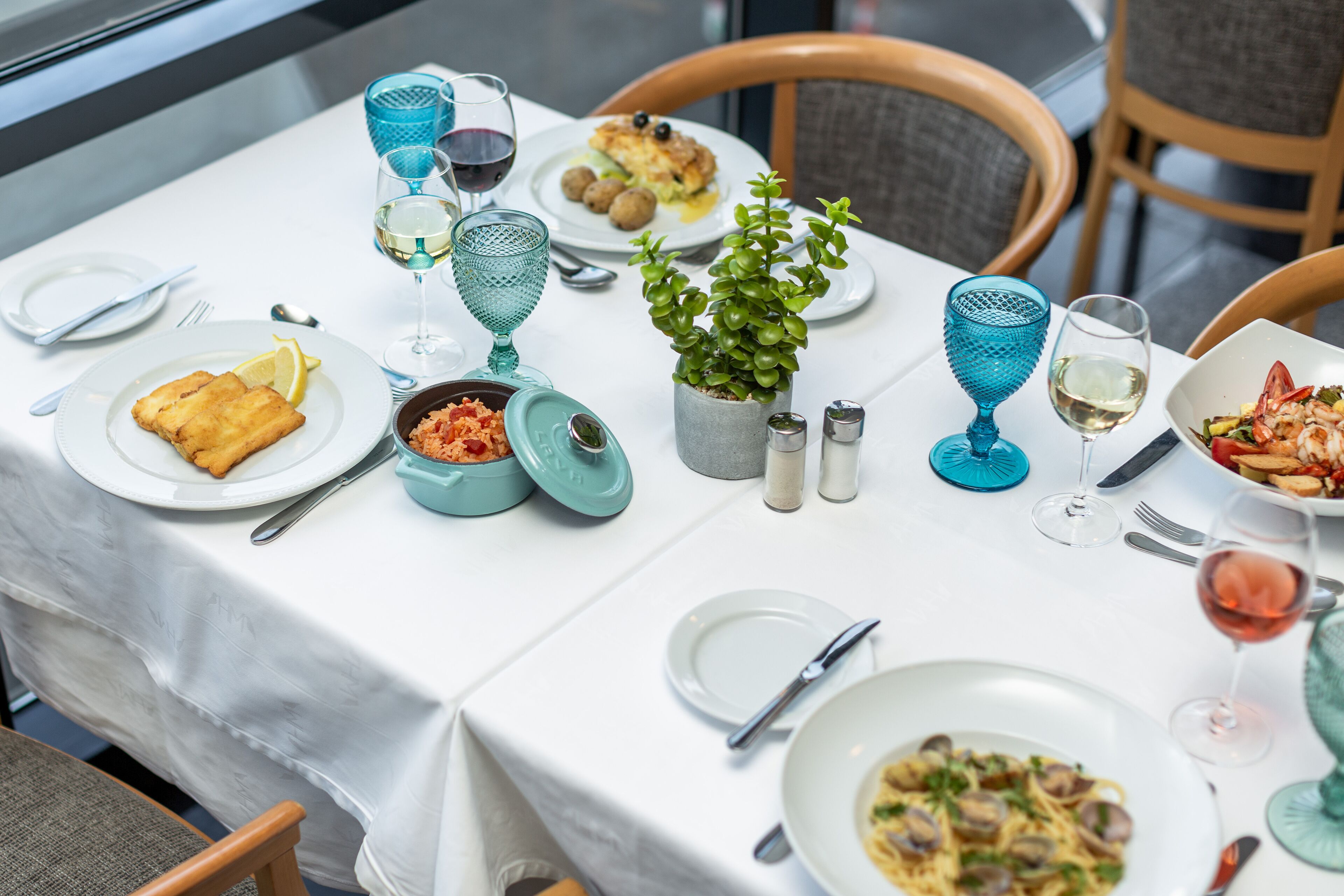 A table set with plates of food, glasses, and a potted plant.