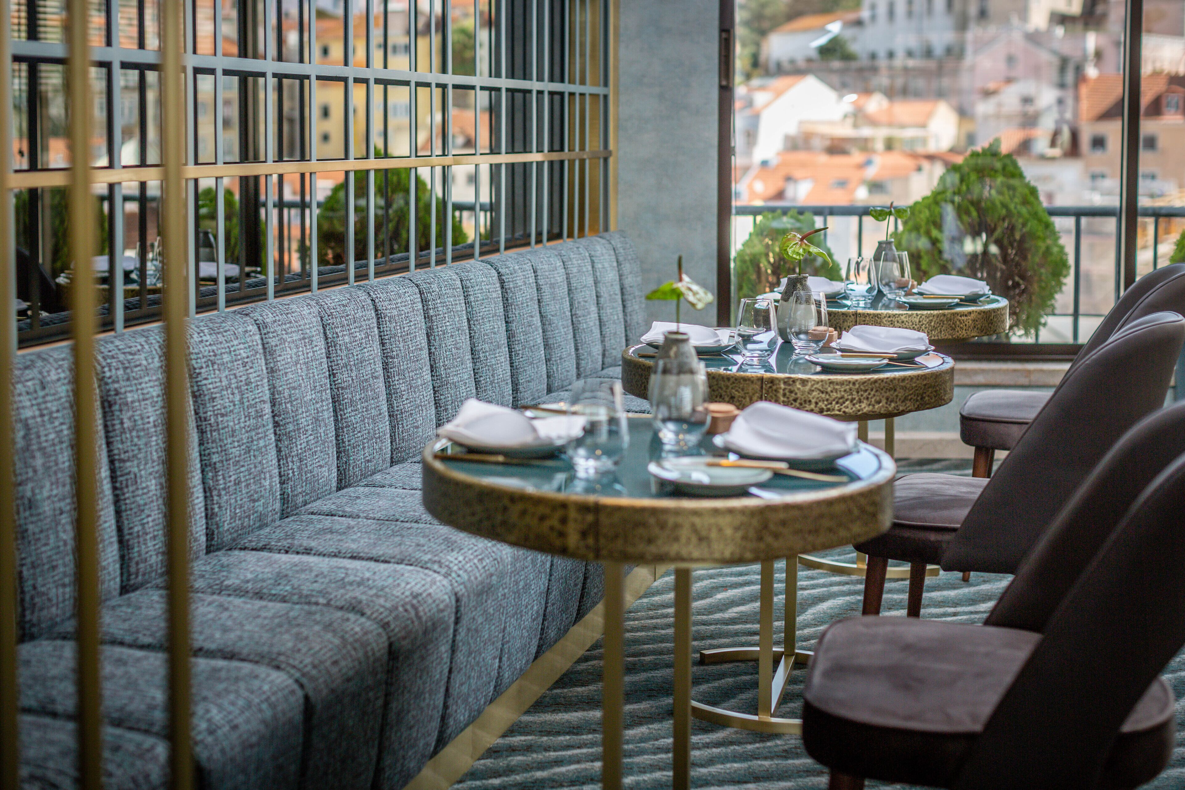 A modern dining area with a sofa and two round tables, each with a small plant and set for dining.