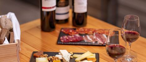 A wooden table with a cheese board, wine glasses, and bottles of wine.