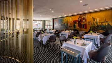 A restaurant with round tables, chairs, and a mural on the wall.