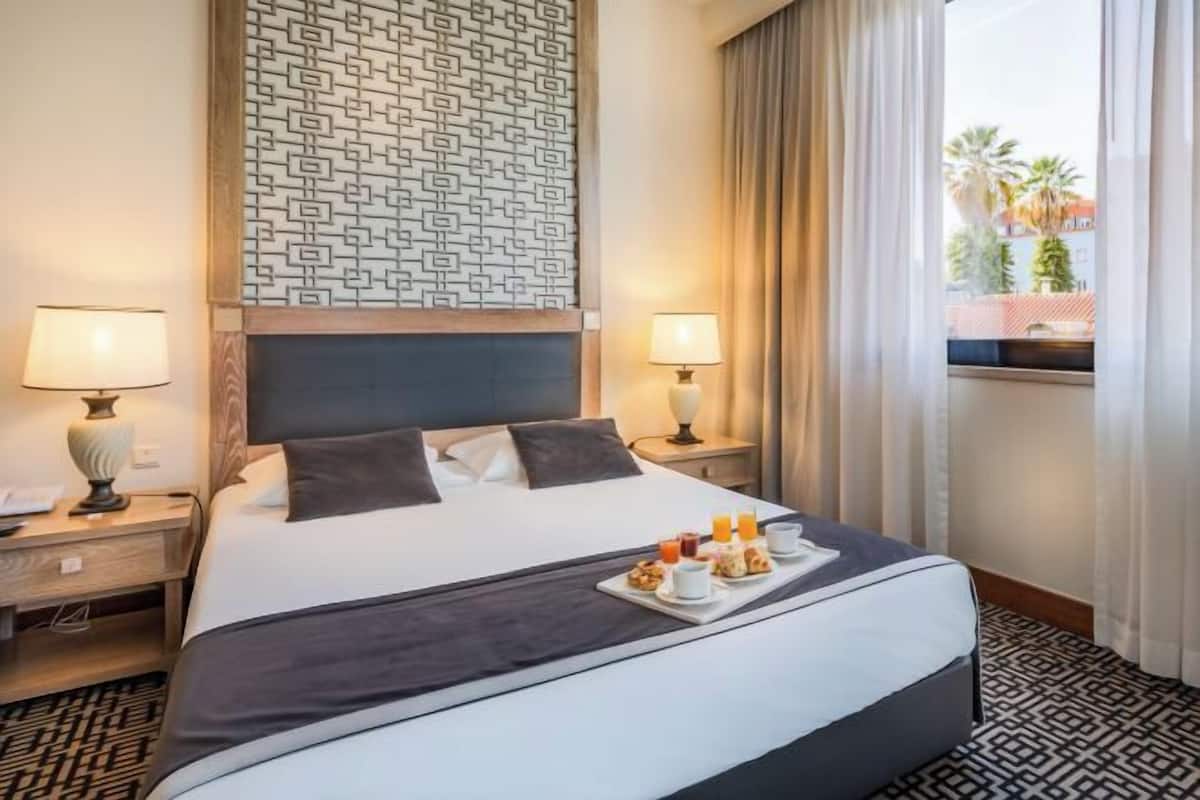 A hotel room with a large bed, two bedside tables with lamps, a tray of breakfast items, and a patterned wall.