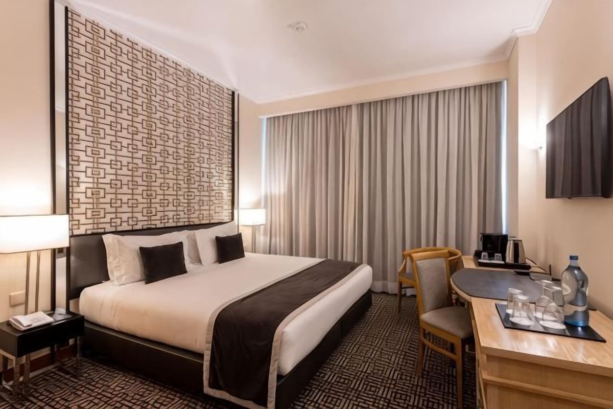 Una habitación de hotel con una cama grande, un escritorio con una silla, un televisor y una ventana con cortinas.
