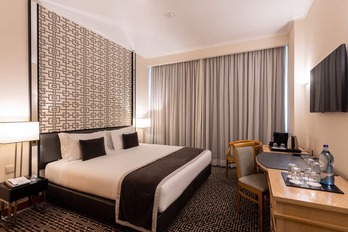 A hotel room with a large bed, a desk with a chair, a television, and a window with curtains.