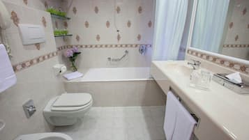 A bathroom with a bathtub, toilet, bidet, and a sink with a mirror.