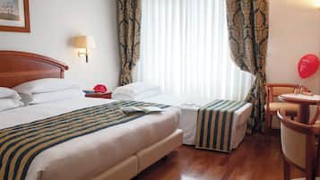 A hotel room with two beds, a bedside table with a lamp, a chair, a small table with a balloon, and a window with curtains.