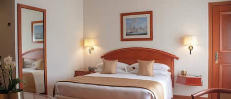 A hotel room with a large bed, bedside lamps, a bedside table, a chair, and a small table with a book.