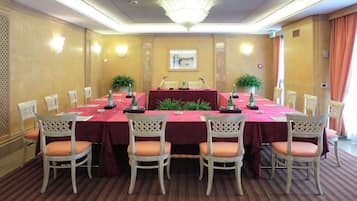 Una sala conferenze con un lungo tavolo, sedie bianche e un lampadario.