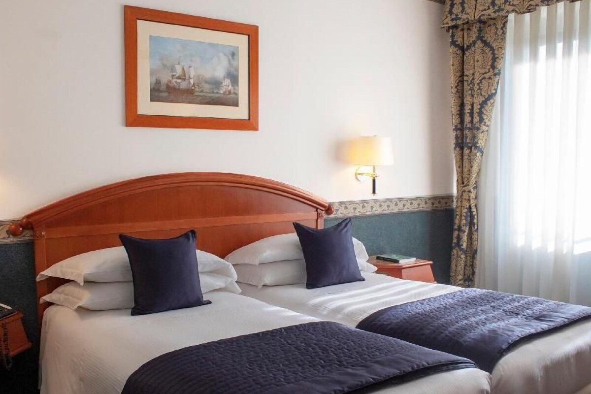 A double bed with a wooden headboard, two pillows, a bedside table with a lamp, and a framed picture on the wall.