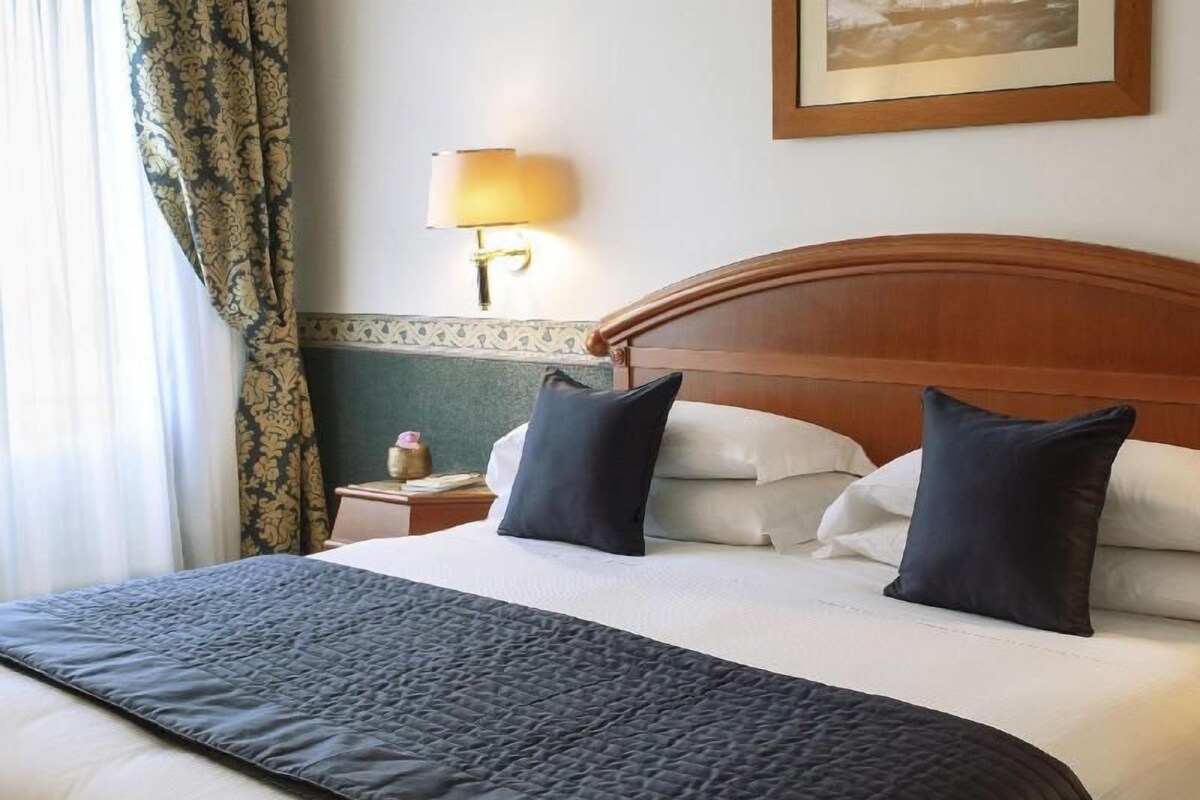 A hotel room with a large bed, a nightstand, a lamp, and a framed picture on the wall.