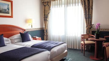 A hotel room with two beds, a desk, a chair, a lamp, and a window with curtains.