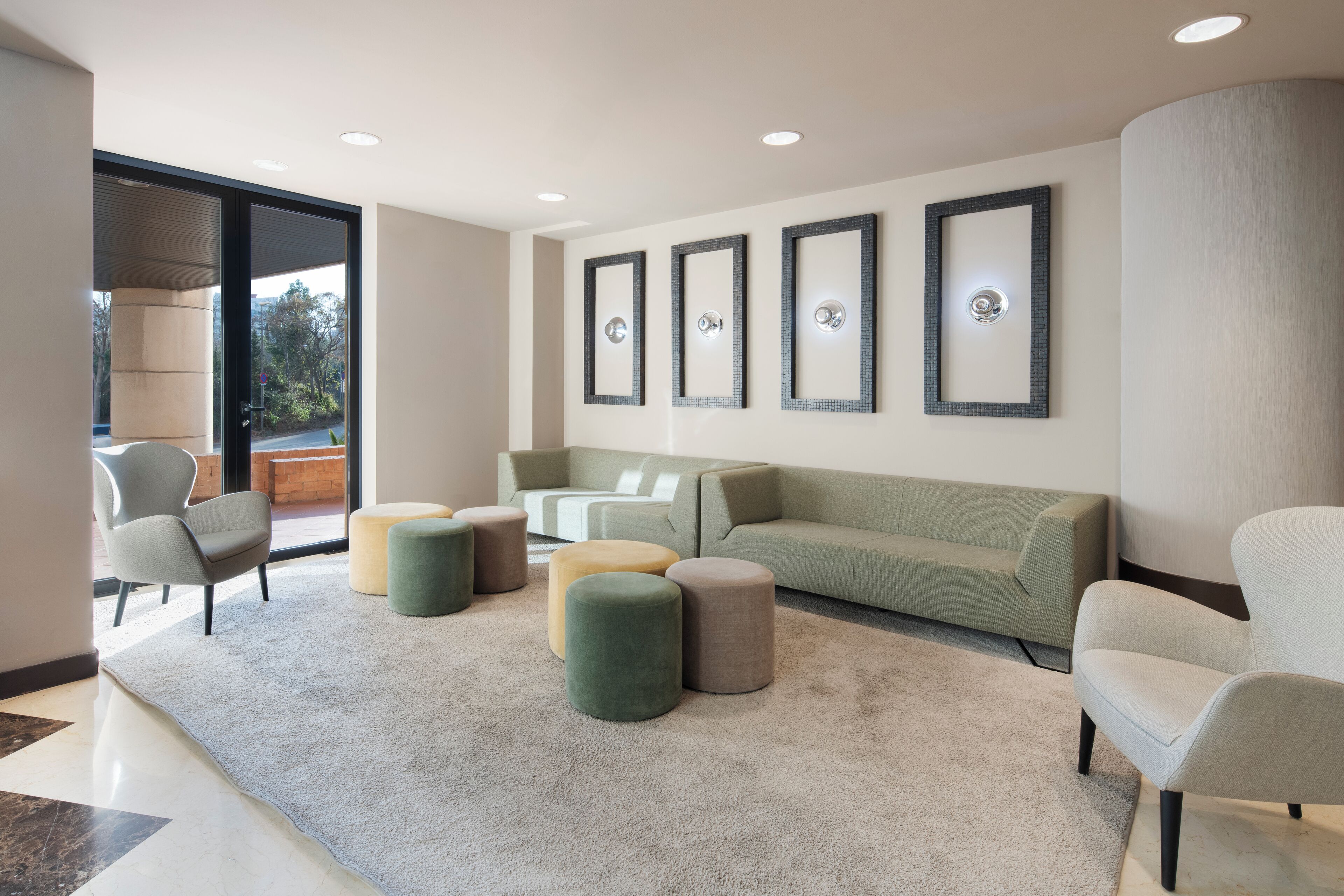 Una sala moderna con un sofá verde, dos sillones y una mesa de centro. Hay tres cuadros enmarcados en la pared y un ventanal con vistas a árboles.