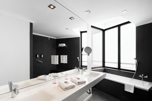 A modern bathroom with a large mirror, two sinks, a bathtub, and a window providing natural light. - Hotel Alimara (Barcelona)