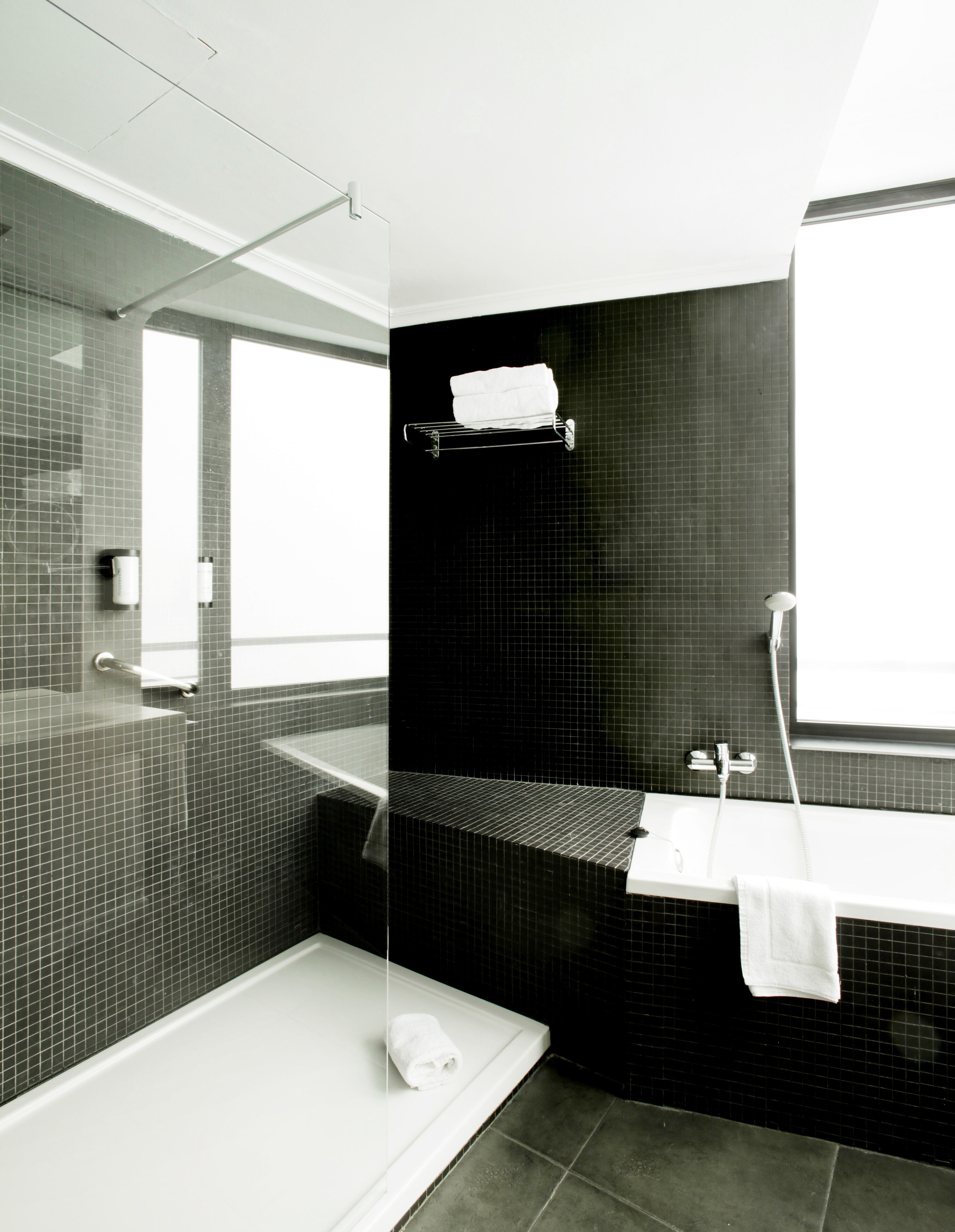 A modern bathroom with a bathtub, a shower, and a sink. There is a towel rack above the sink and a window providing natural light.