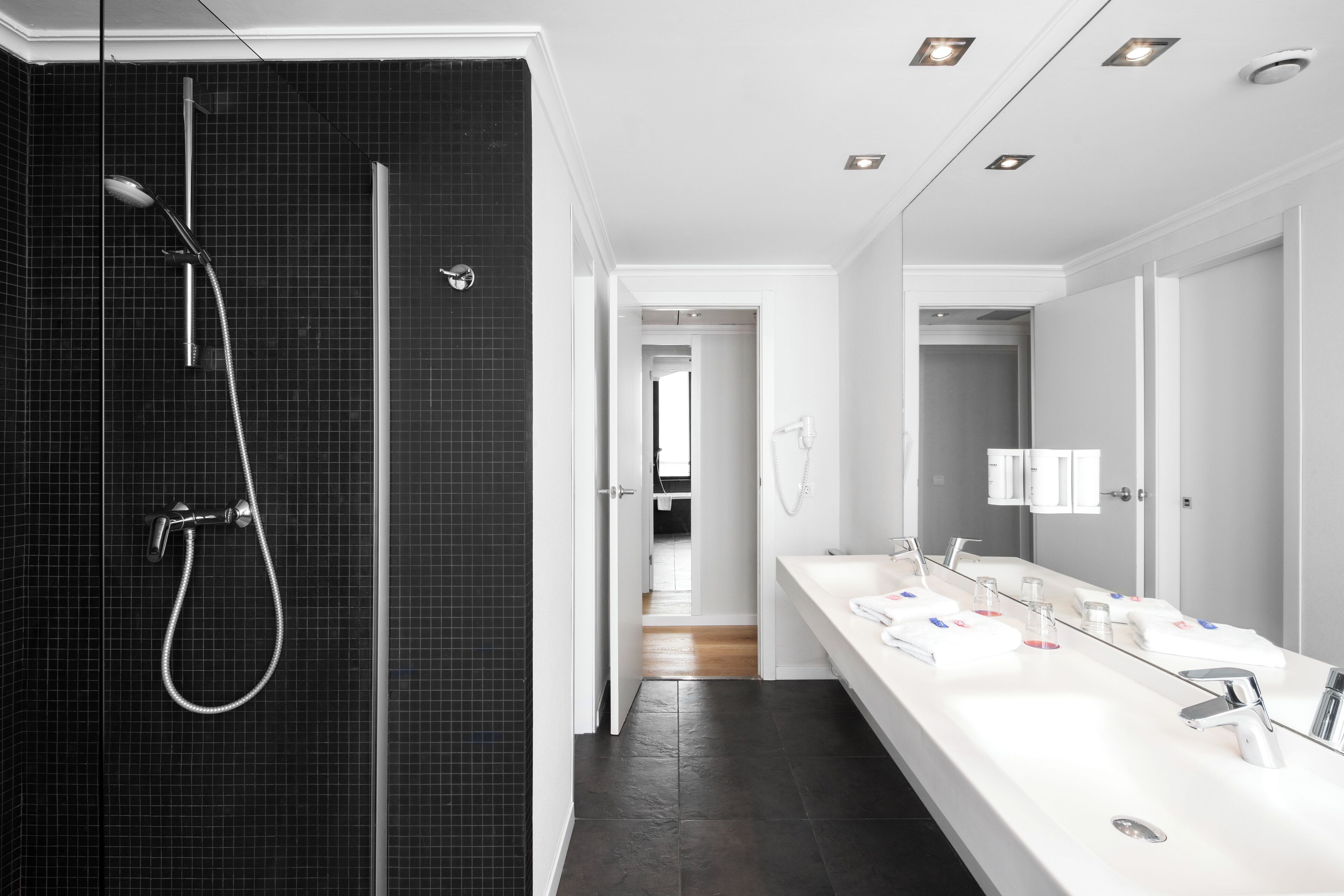 Un baño moderno con ducha de vidrio, lavamanos blanco con múltiples grifos y un espejo grande.