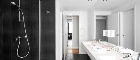Un baño moderno con ducha de vidrio, lavamanos blanco con múltiples grifos y un espejo grande.