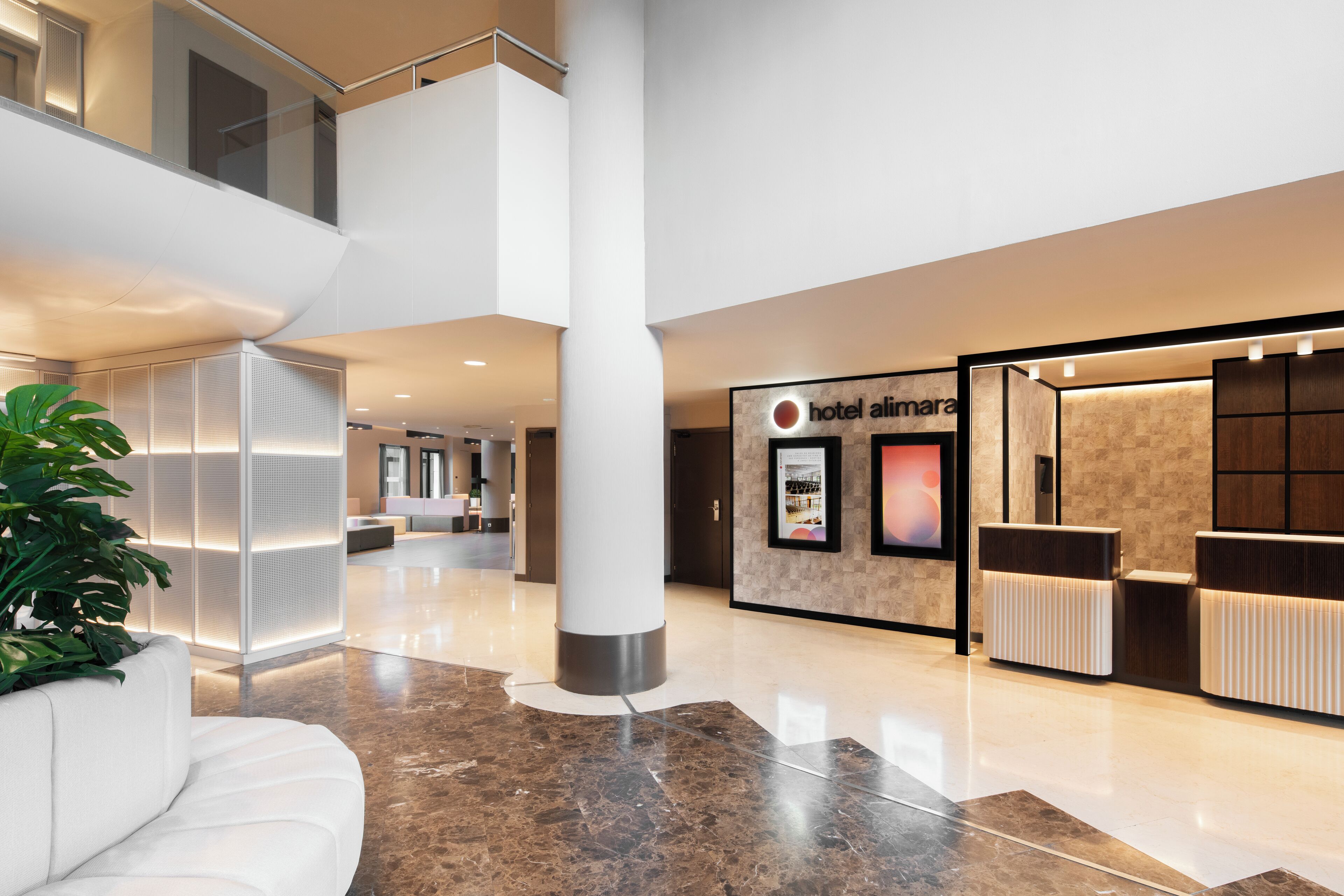 Un hall d’hôtel moderne avec un comptoir d’accueil, un espace salon et une grande plante.